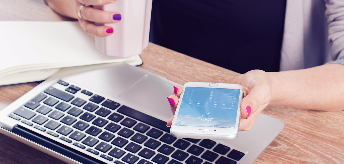 Woman checking out the weather on her iPhone with an open MacBook